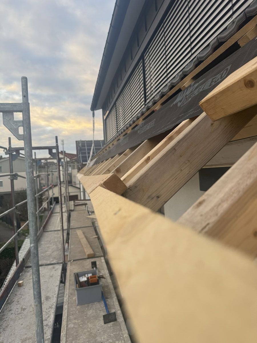 Eine Ansicht aus der Froschperspektive von einem Gerüst aus zeigt die Montage neuer hölzerner Dachsparren an der Seite eines Gebäudes.