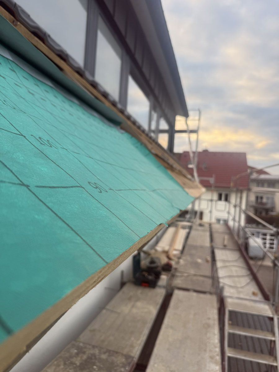 Nahaufnahme einer türkisfarbenen, gitterförmigen Dachunterlage, die von einem Baugerüst aus auf einem Schrägdach verlegt wird.