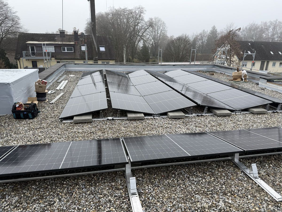 Auf einem flachen, mit Kies bedeckten Dach wurden Solarpaneele installiert, wobei einige Paneele schräg angeordnet und andere flach in Reihen verlegt waren.