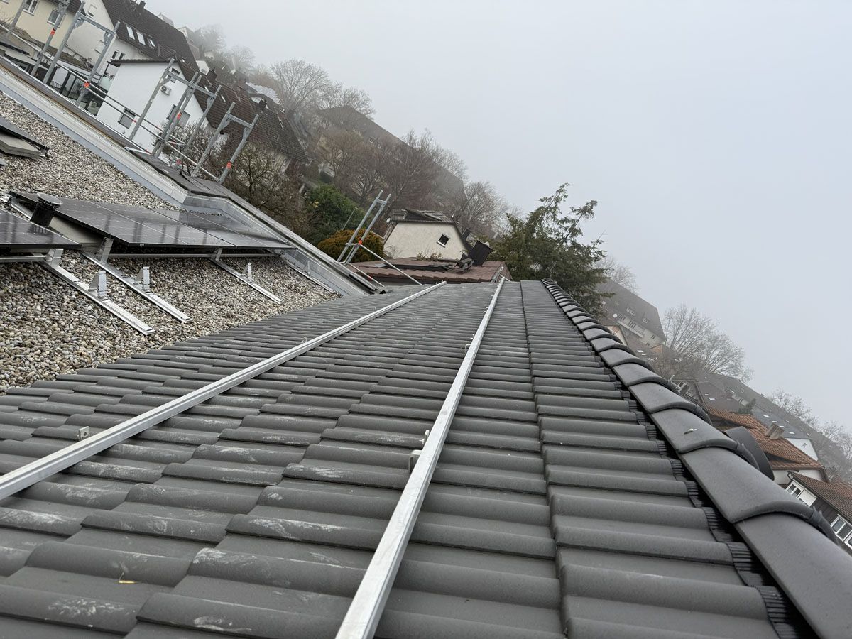Metallische Montageschienen wurden während der Installation einer Solaranlage auf einem grauen Ziegeldach angebracht.