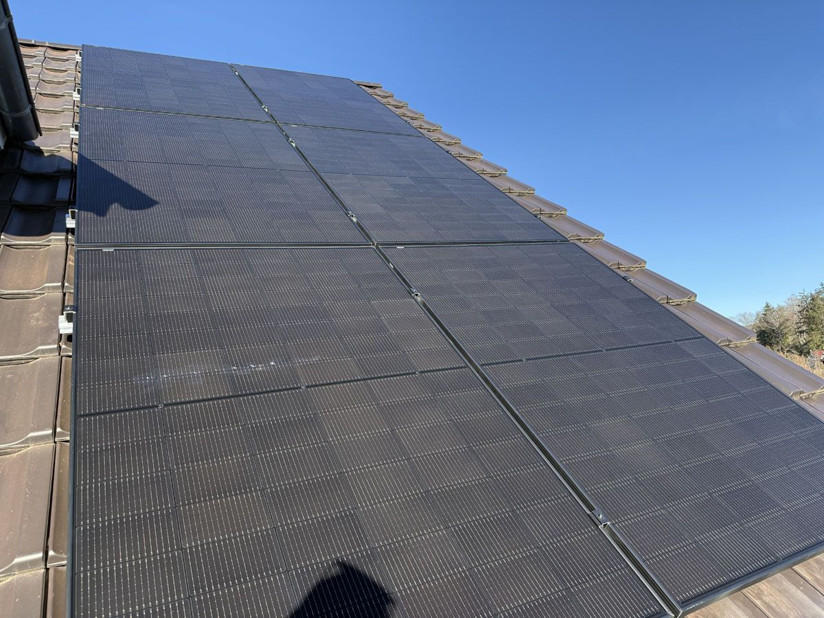 Ein Raster aus schwarzen Solarzellen, installiert auf einem schrägen Dach mit grauen Ziegeln, vor einem klaren blauen Himmel.