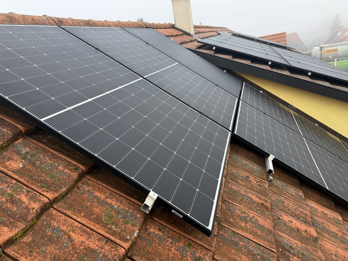 Solarpaneele wurden an einem bewölkten Tag auf einem verwitterten, rotbraunen Ziegeldach installiert.