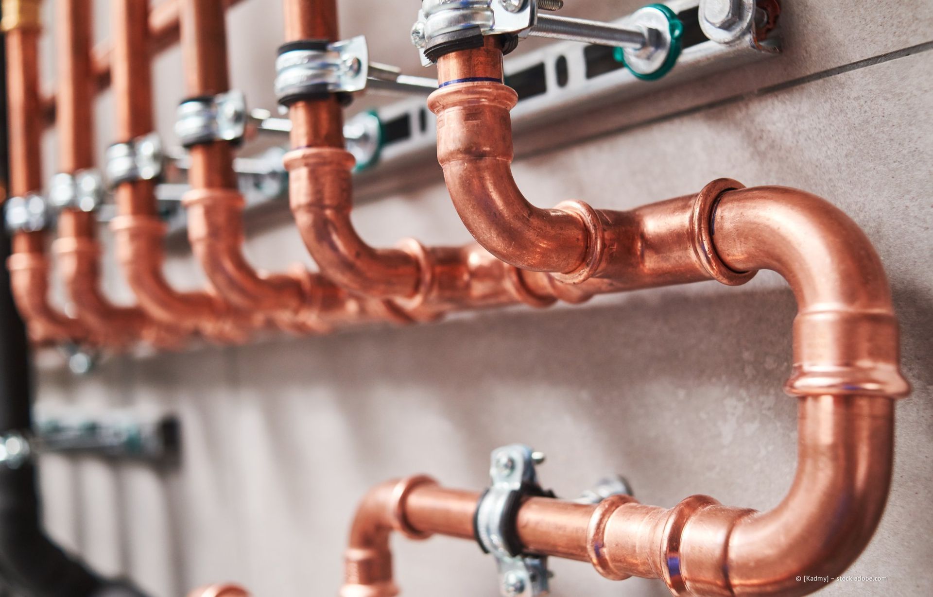 An einer Wand installierte Kupferrohre mit Klemmen und Winkelstücken.