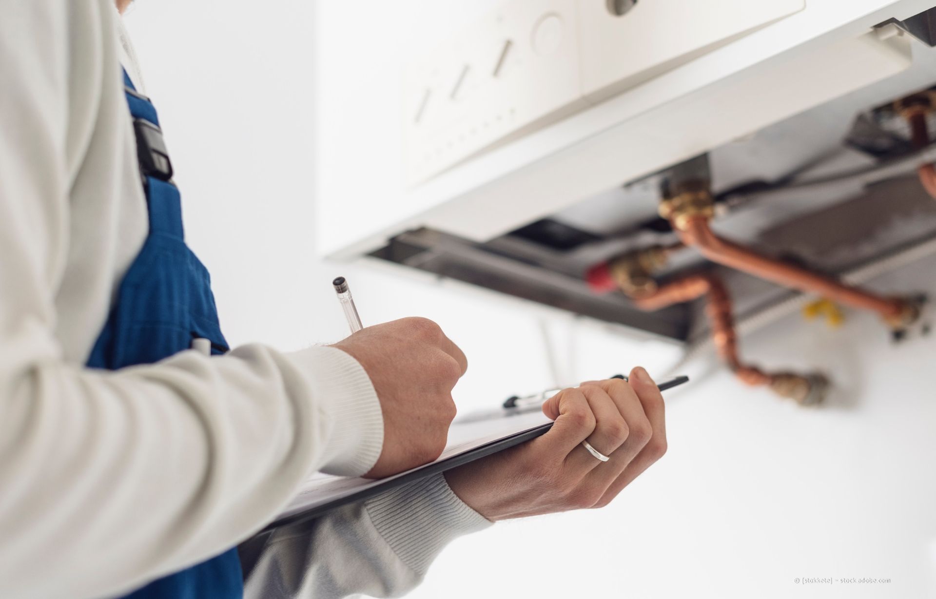 Techniker inspiziert einen Heizkessel und macht sich Notizen auf einem Klemmbrett.