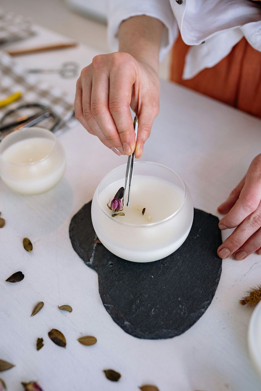 Persona haciendo una vela, usando pinzas para agregar pétalos de rosa a la 