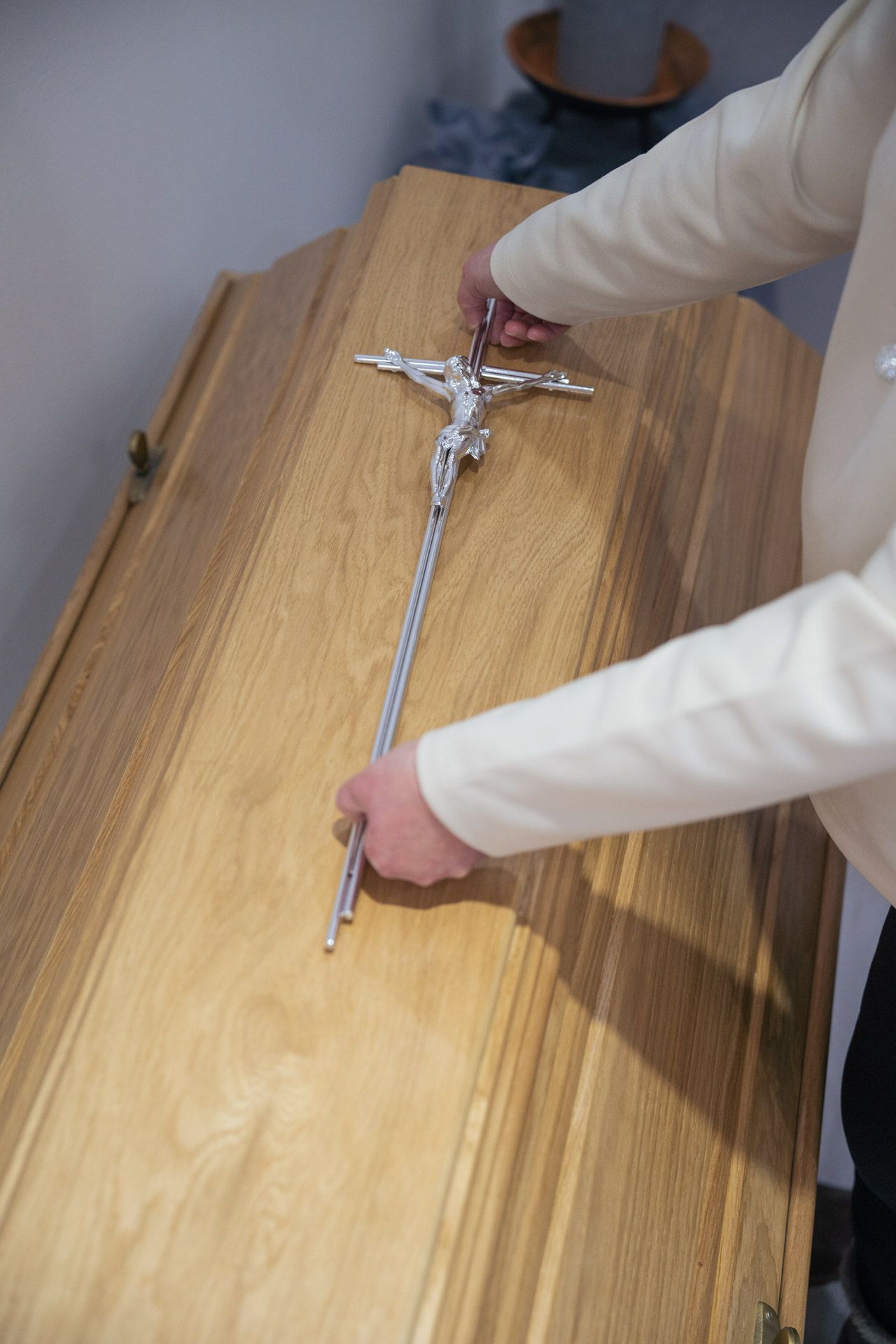 Auf eienn Sarg wird ein silberndes Kreuz gelegt.