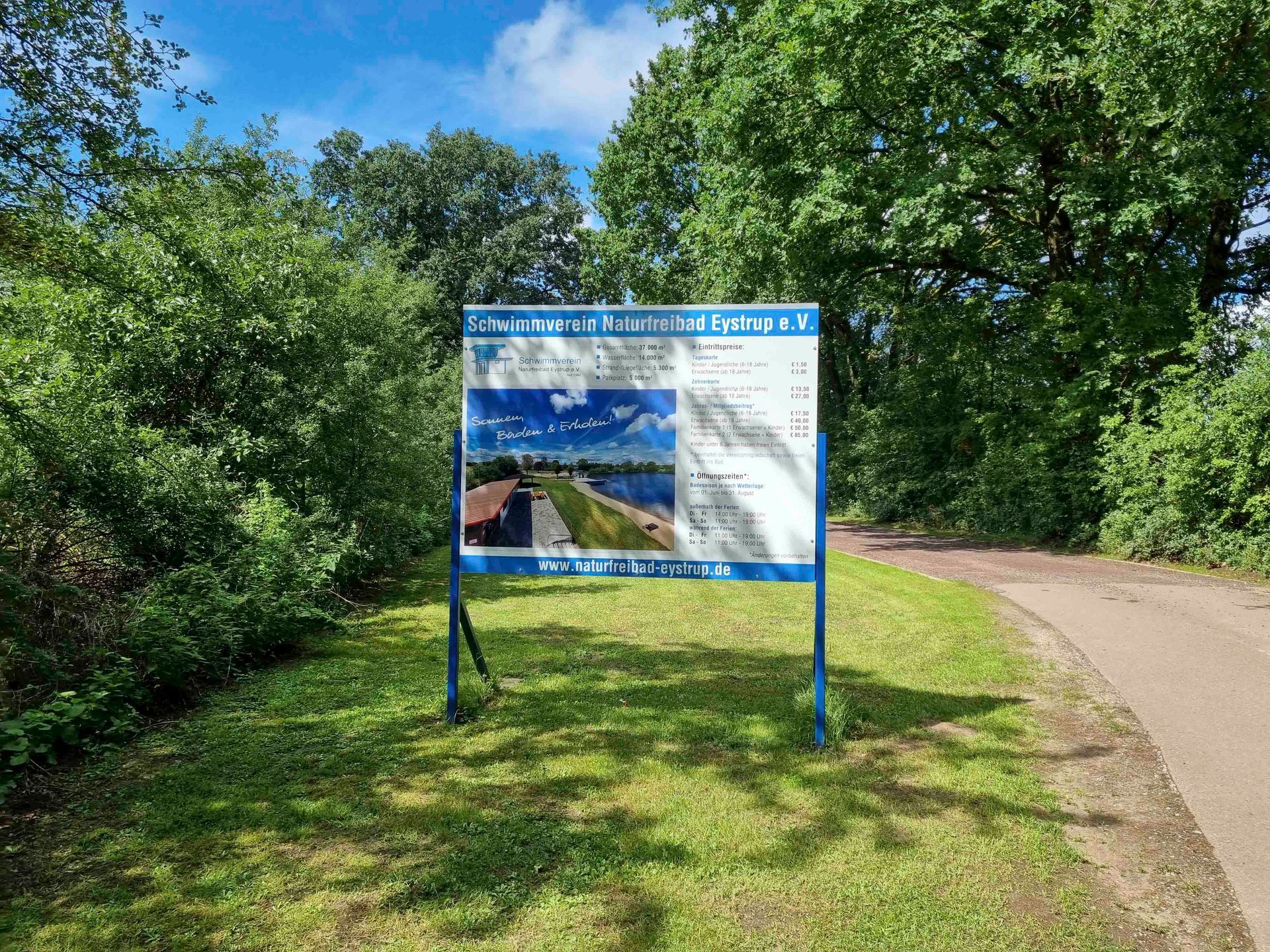 Ein blau-weißes Schild steht mitten auf einer Wiese.