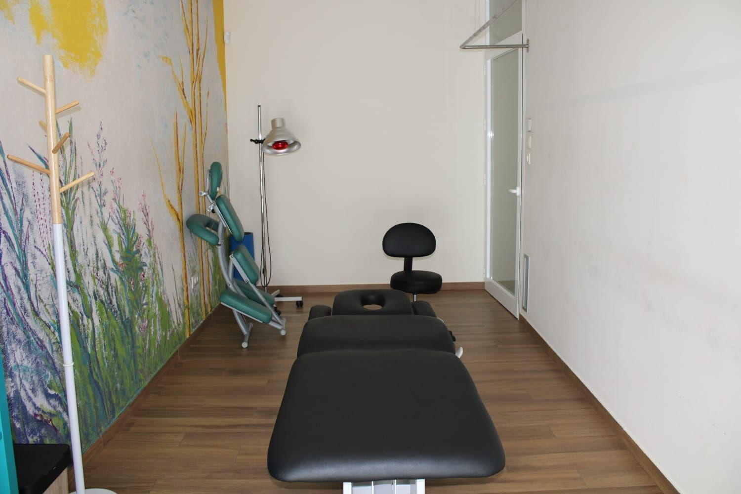 Sala de tratamientos con camilla, silla y equipo de masaje. Mural y suelo de madera.