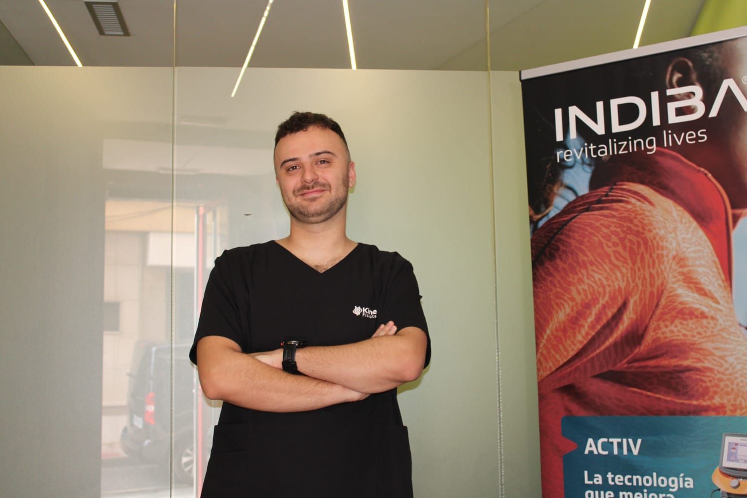 Hombre con uniforme negro y brazos cruzados, de pie cerca de una pancarta de INDIBIA.