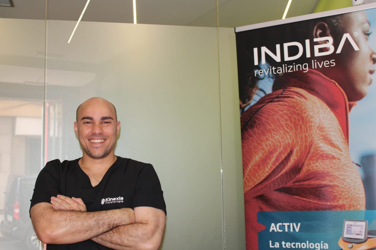 Hombre con los brazos cruzados sonriendo junto a una pancarta de 