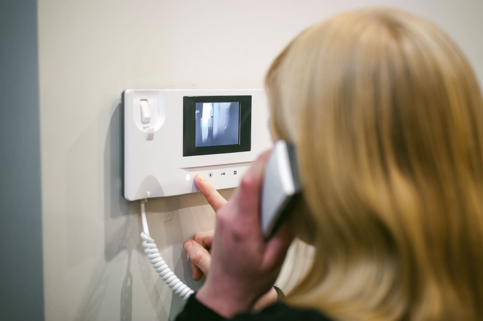 Eine Person benutzt eine an der Wand montierte Video-Gegensprechanlage und zeigt auf den Bildschirm.