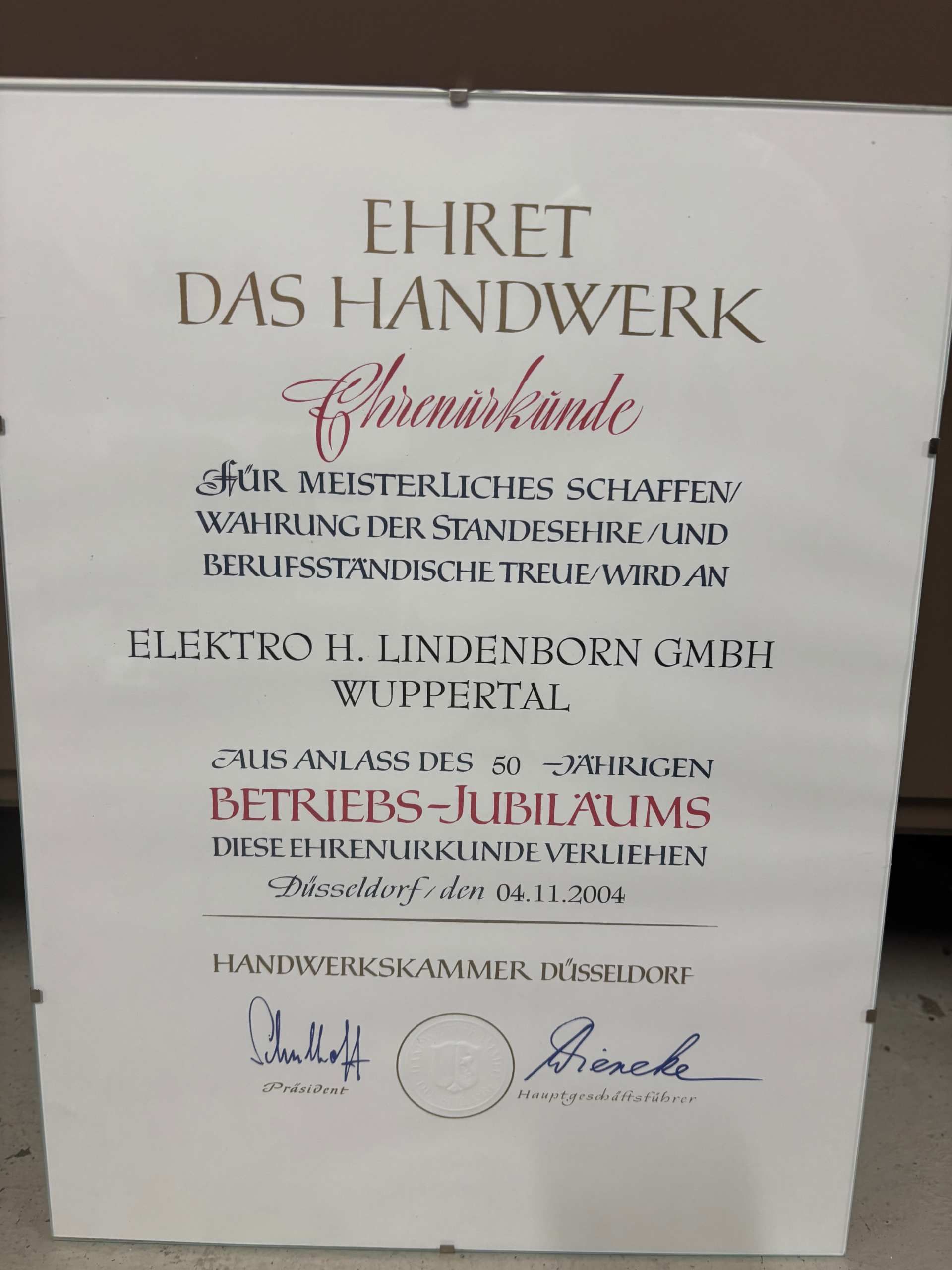 Plakat mit deutschem Text in Schwarz und Rot auf weißem Hintergrund, das für ein Unternehmen oder eine Veranstaltung wirbt.