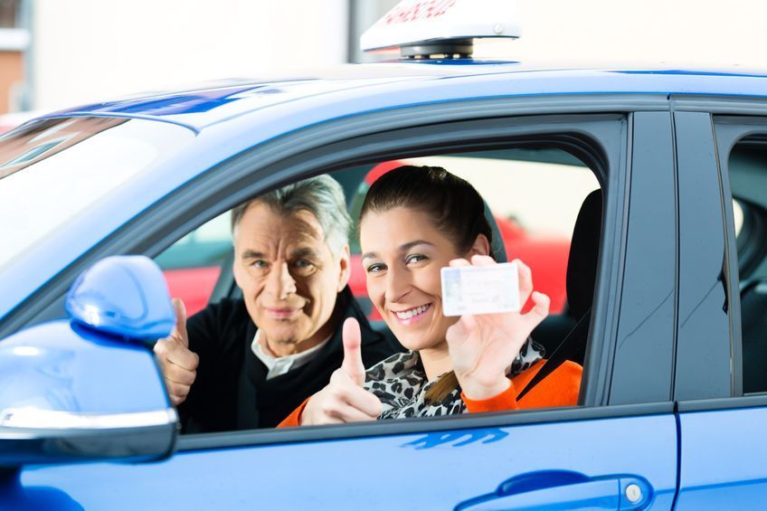 Dos personas en un coche azul, sonriendo y mostrando una tarjeta por la ventanilla abierta