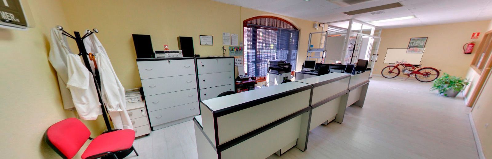 Luminoso vestíbulo de oficina con escritorios, archivadores, sillas y un mostrador con ventanilla