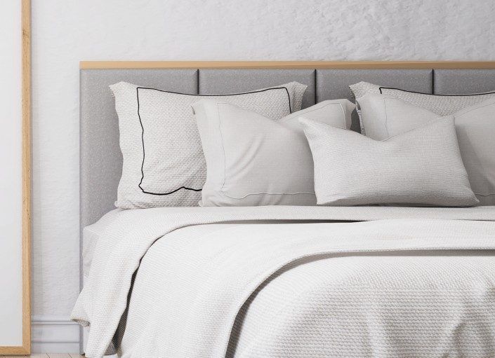 Lit avec draps blancs et tête de lit grise ; oreillers disposés.