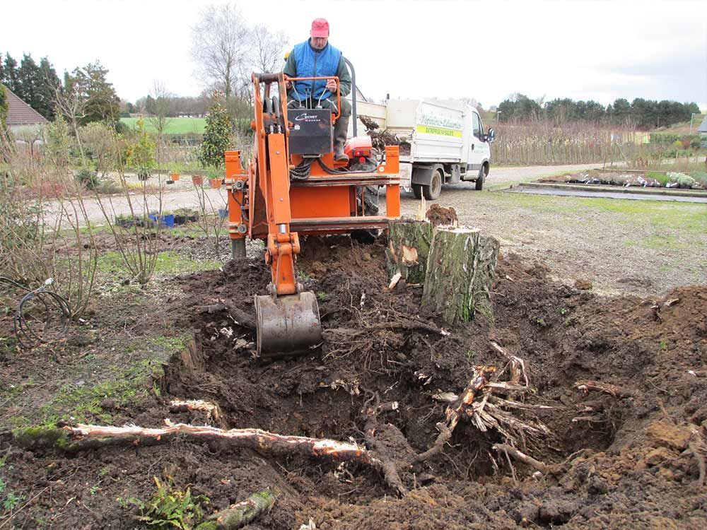 Une excavatrice déblaye un terrain boueux, avec un ouvrier sur la machine et un camion en arrière-plan.