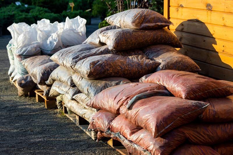 Sacs de terre ou de céréales empilés sur des palettes en bois à l'extérieur, près d'une clôture