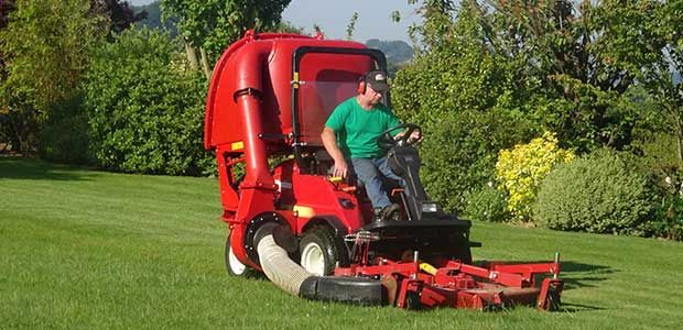 Un homme conduit une tondeuse à gazon rouge sur une pelouse verte dans un jardin ensoleillé
