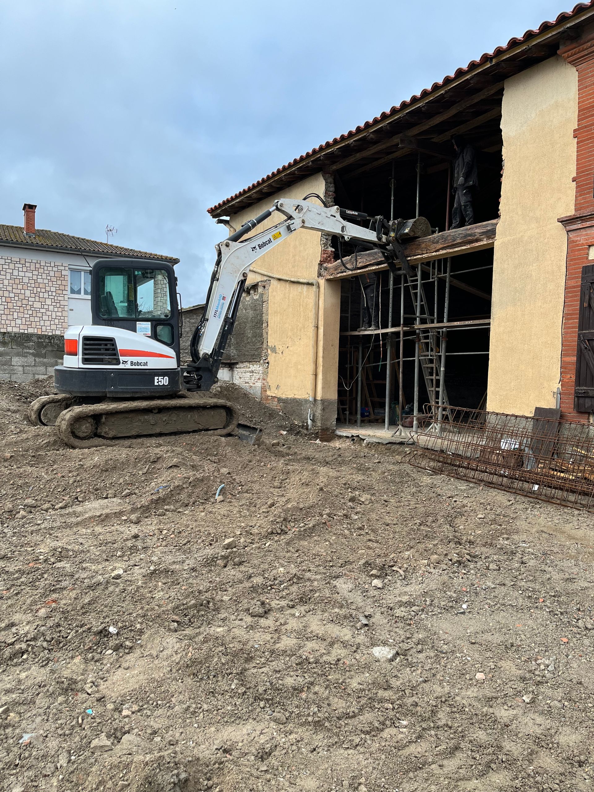 Une pelleteuse avec un bras mécanique qui touche un mur de maison