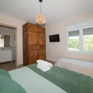 Dormitorio con cama, armario, TV y ventana con vista a un paisaje verde.