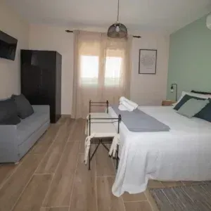 Dormitorio con cama, sofá, armario, dos sillas y una ventana.