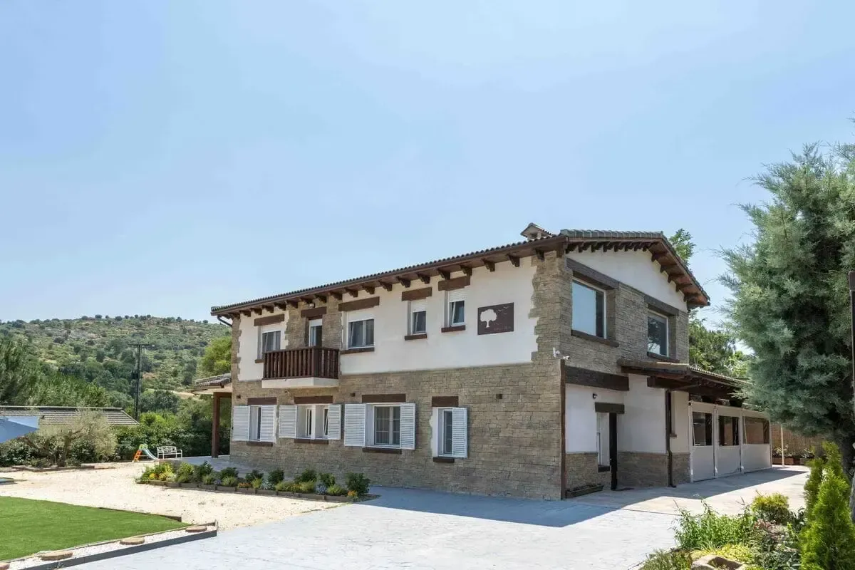 Casa de piedra de dos pisos con balcón, contraventanas y molduras marrones en un día soleado.