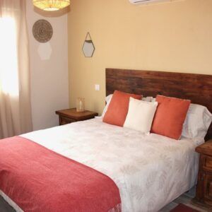 Dormitorio con cama, cabecero, mesitas de noche y cojines decorativos en tonos naranja y blanco.
