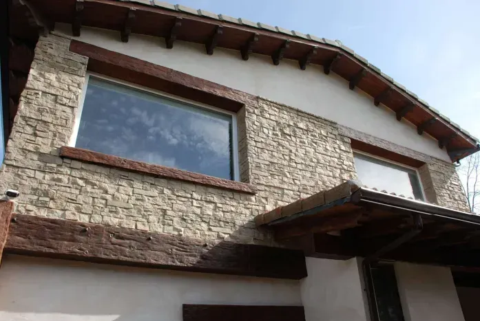 Exterior de un edificio con fachada de piedra, dos ventanas y vigas de madera oscura.