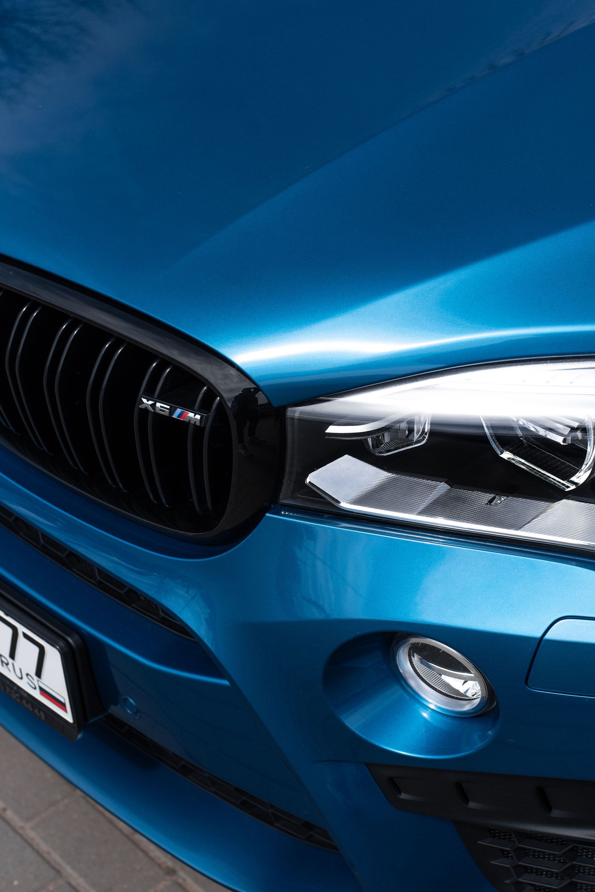 Primer plano de la parrilla delantera y el faro de un BMW azul con acabado brillante.