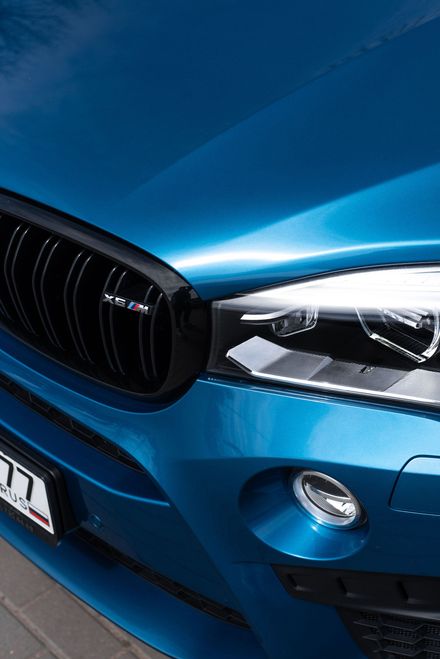Primer plano de la parrilla delantera y el faro de un BMW azul con acabado brillante.