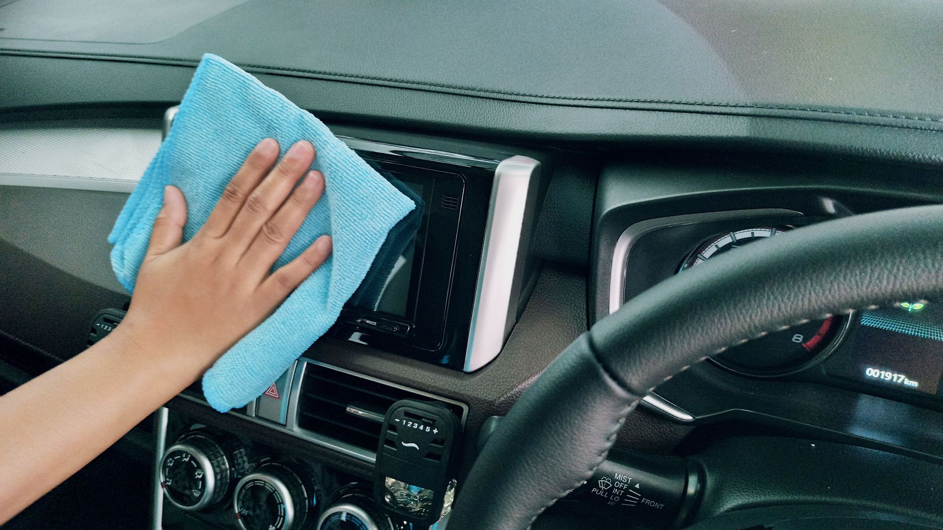 Limpiar a mano el salpicadero de un coche con un paño azul cerca de la consola central y las rejillas de ventilación.