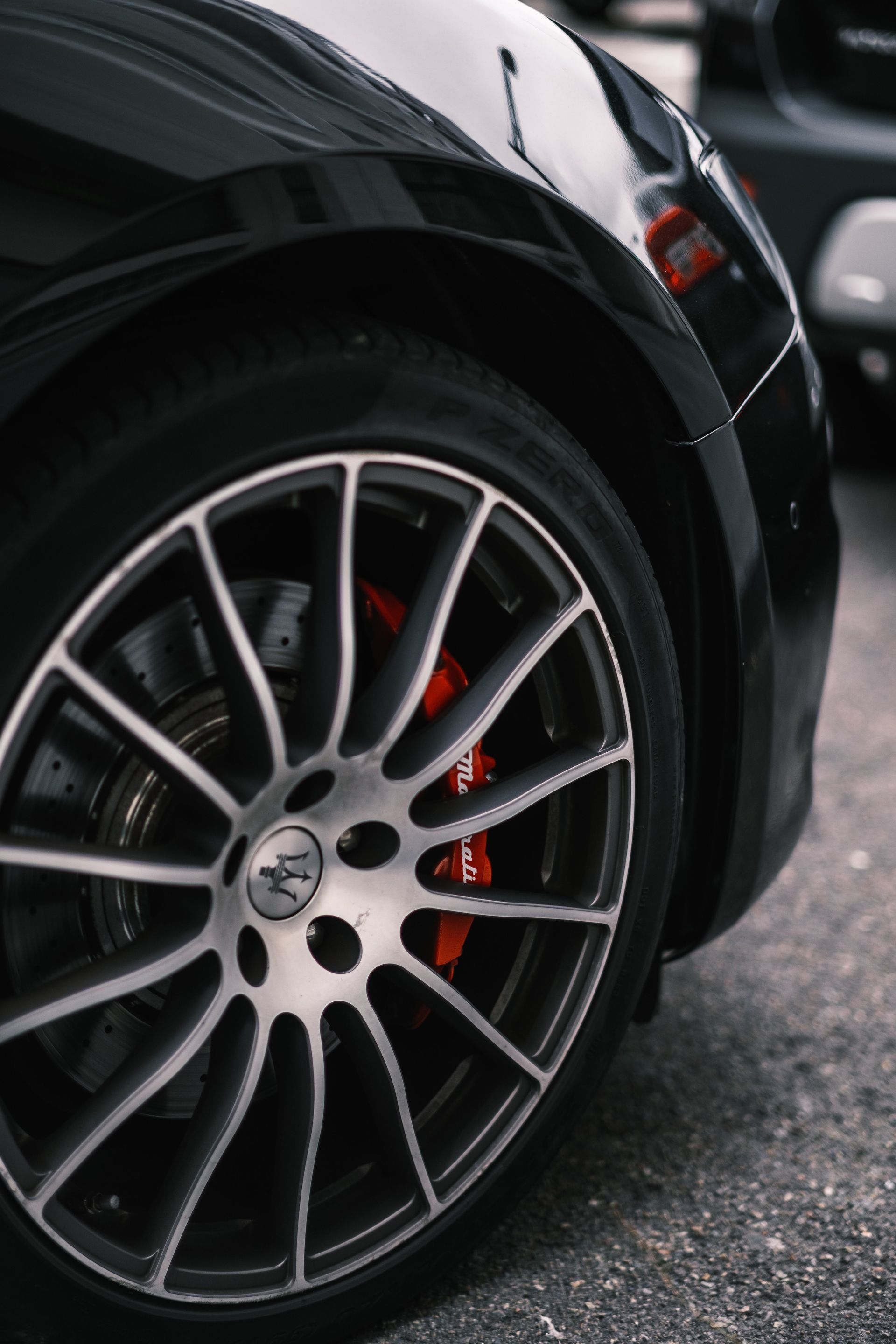 Primer plano de la rueda delantera de un coche deportivo negro con llanta de aleación plateada y pinza de freno roja 