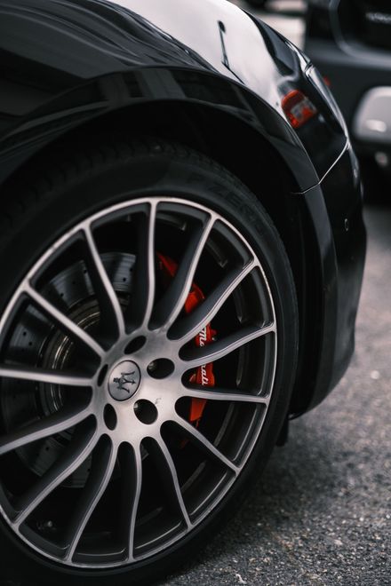 Primer plano de la rueda delantera de un coche deportivo negro con llanta de aleación plateada y pinza de freno roja 