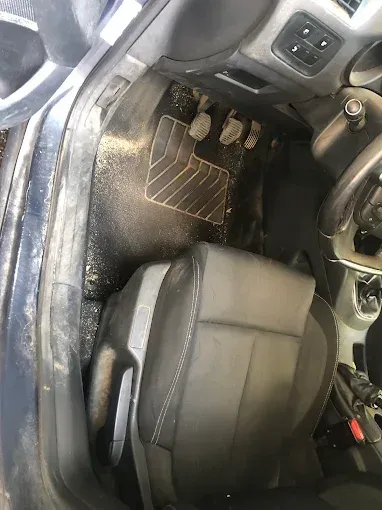 Espacio para los pies del coche con pedales y asiento del conductor, mostrando la alfombrilla y el marco de la puerta 