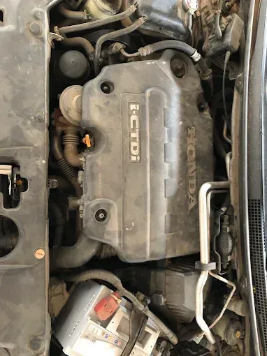 Primer plano del compartimento del motor de un coche con la tapa del motor Honda y la batería visibles.