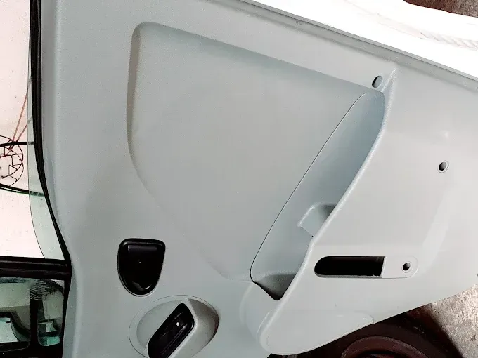 Interior de un panel de puerta de coche blanco con manija, controles de ventana y bolsillo de almacenamiento.