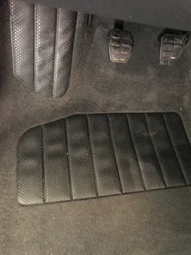 Espacio para los pies del coche con alfombrilla de goma negra y pedales visibles encima.