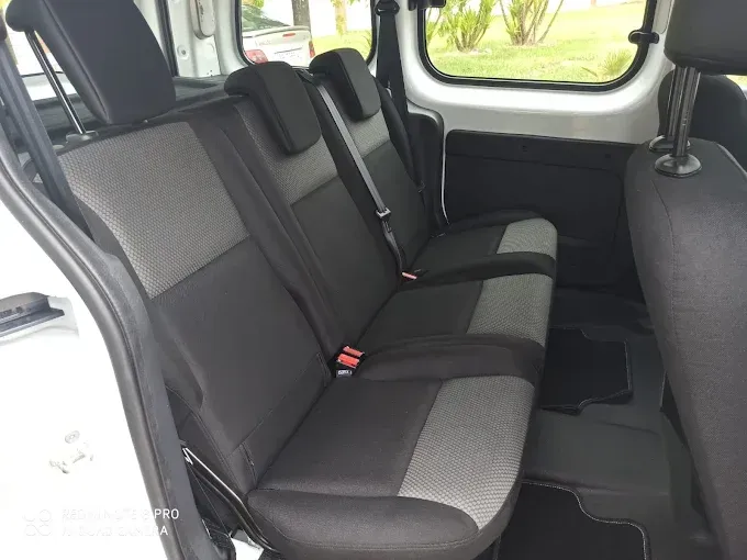 Asiento trasero de un coche con banco y reposacabezas de tela gris, visto desde un lateral a través de una puerta abierta.