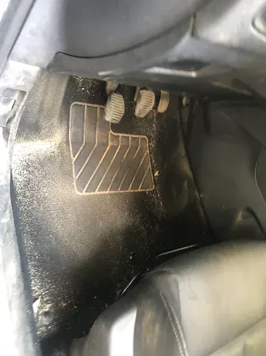 Primer plano de tres pedales de coche con una alfombrilla negra y una zona de apoyo del talón con contorno blanco.