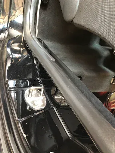 Primer plano de la bisagra de la puerta de un coche y el embellecedor negro junto a un asiento gris.