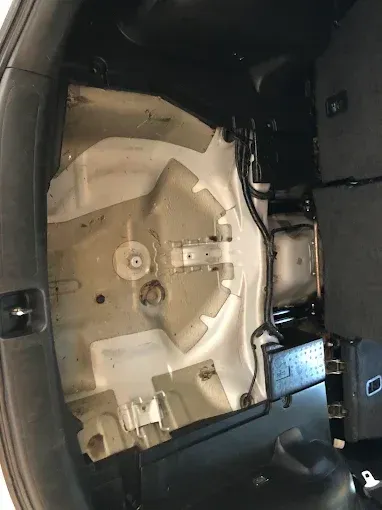 Interior del maletero del coche con compartimento para la rueda de repuesto y paneles beige y negros a la vista.