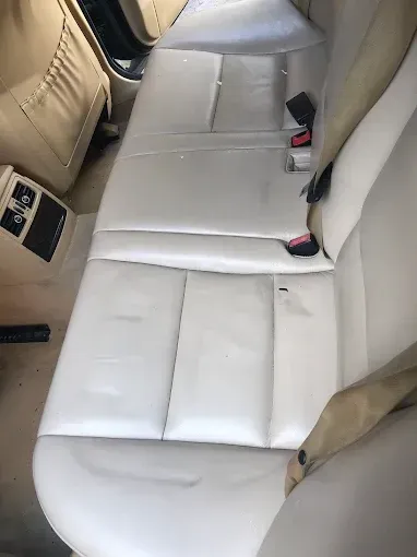 Asiento trasero de cuero beige de un coche con dos cinturones de seguridad visibles.