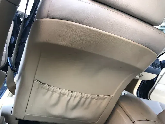 Parte trasera de un asiento de coche beige con un pequeño bolsillo de almacenamiento y costuras visibles.