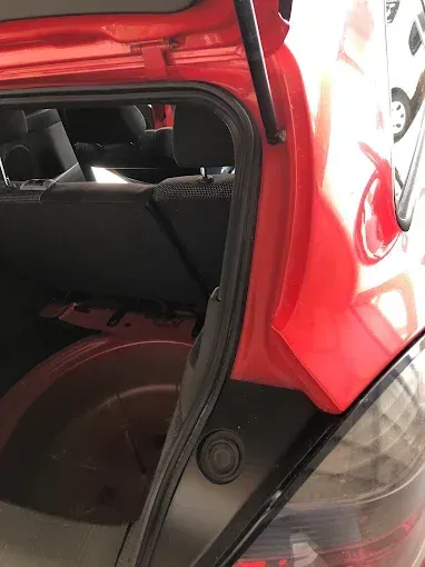 Portón trasero de coche rojo abierto con la zona de los asientos traseros visible y el maletero entreabierto