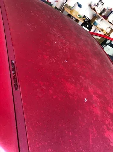 Primer plano del capó rojo polvoriento de un coche en un garaje.