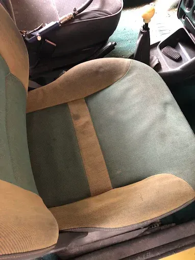 Primer plano de un asiento de coche con tapicería verde y beige y una bolsa negra al lado.
