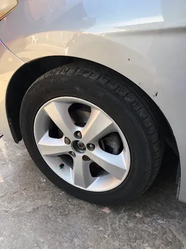 Primer plano de la rueda trasera y el neumático de un coche plateado sobre una entrada de hormigón.