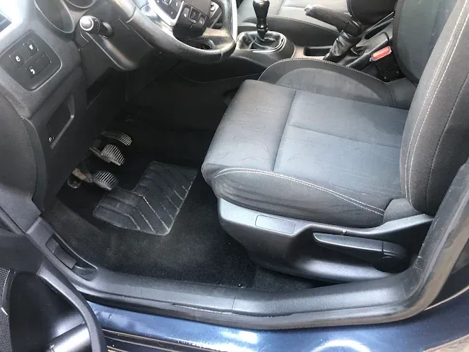Interior del coche con el asiento delantero, el volante, la consola central y la alfombrilla de goma de color gris 