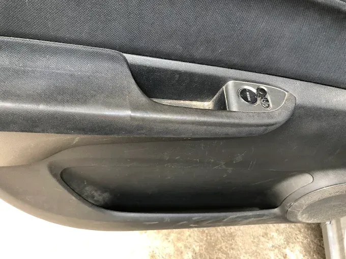 Primer plano del interior de la puerta de un coche con manija negra y pestillo de cierre plateado.