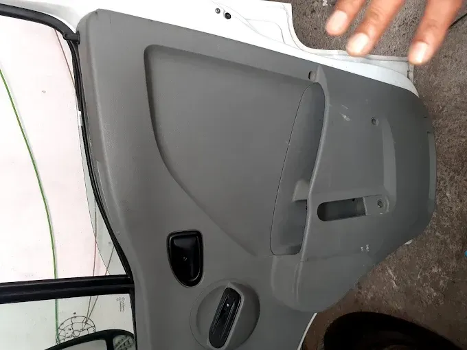 Panel interior de la puerta de un coche de color gris, con manivela y tirador para la ventanilla, fotografiado en interiores.